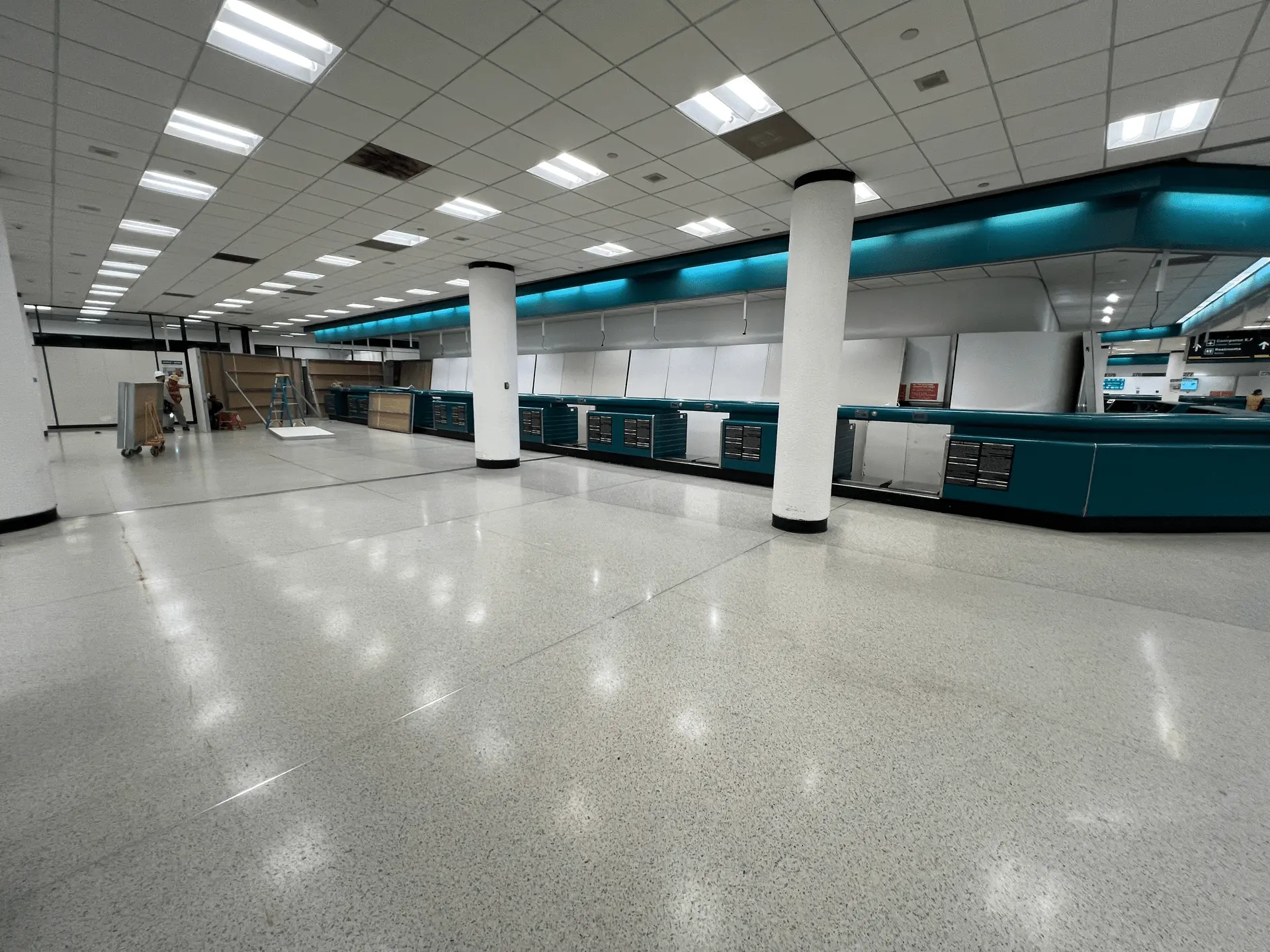 The same counter area mid-demolition, showing the original teal-paneled check-in desks stripped out and under active construction ahead of the buildout.